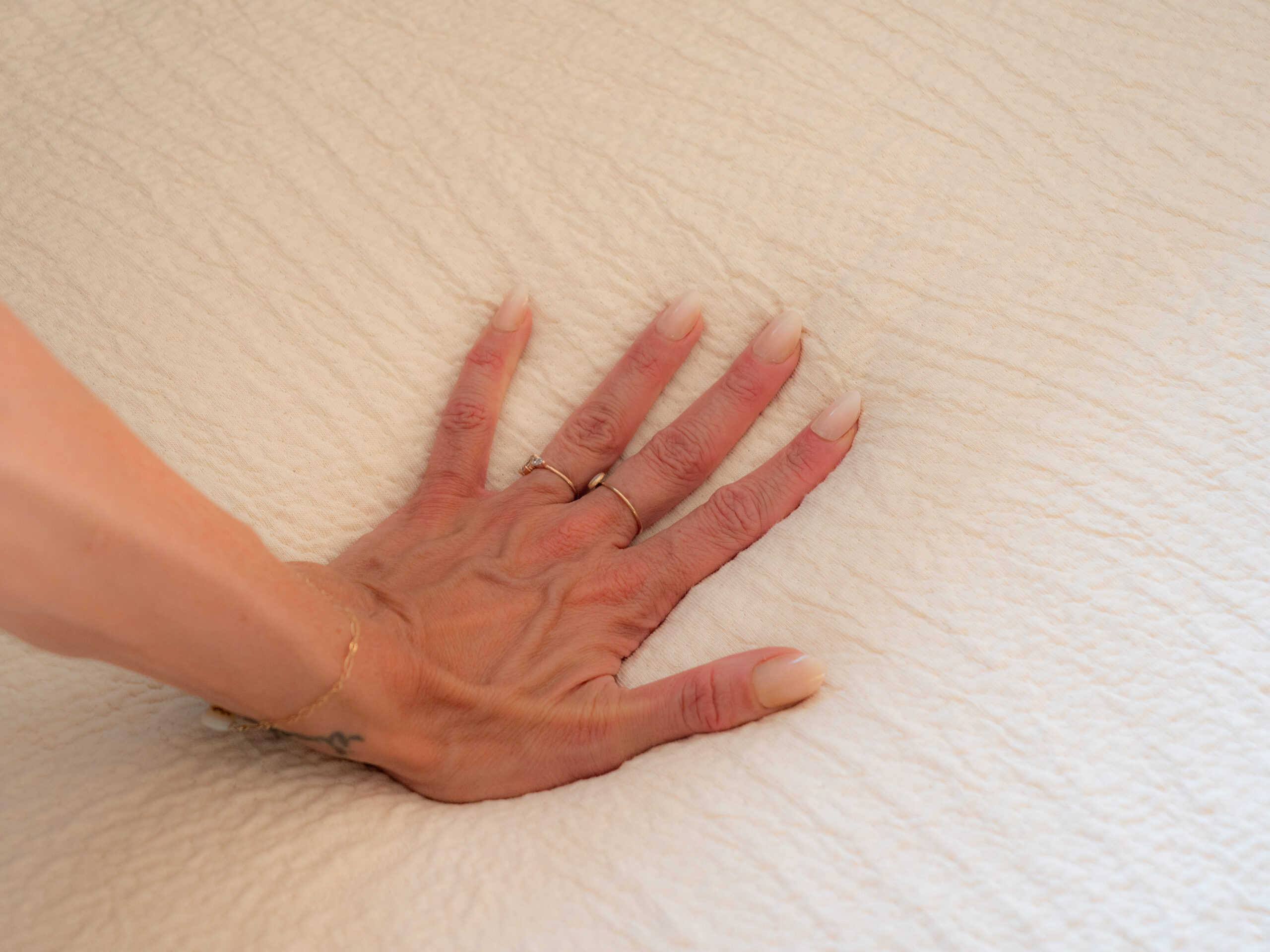 A hand with manicured nails presses down on a textured, light-colored fabric surface, causing a visible indentation.