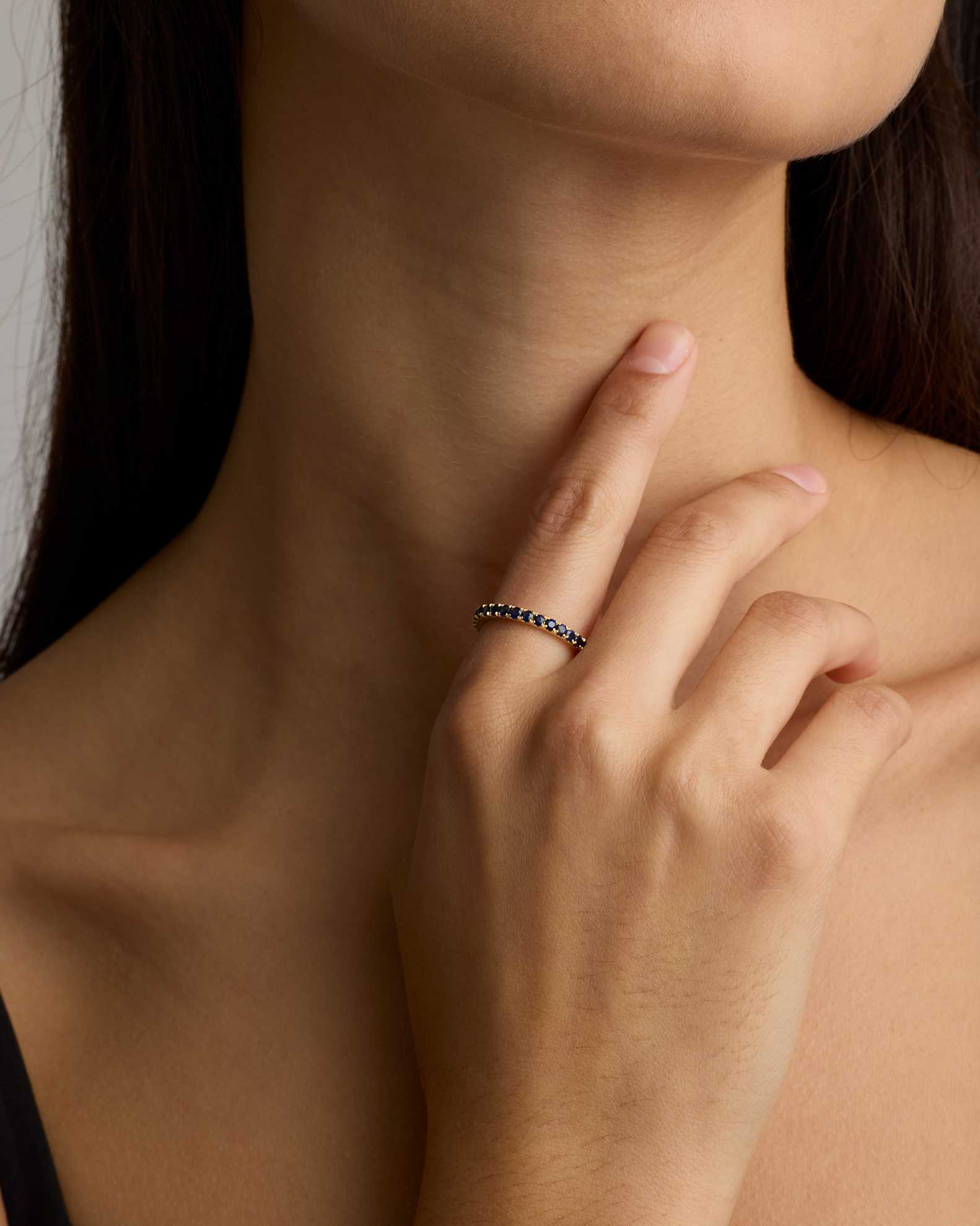 A person touches their chin with their index finger, wearing a thin ring set with small dark stones on their ring finger.