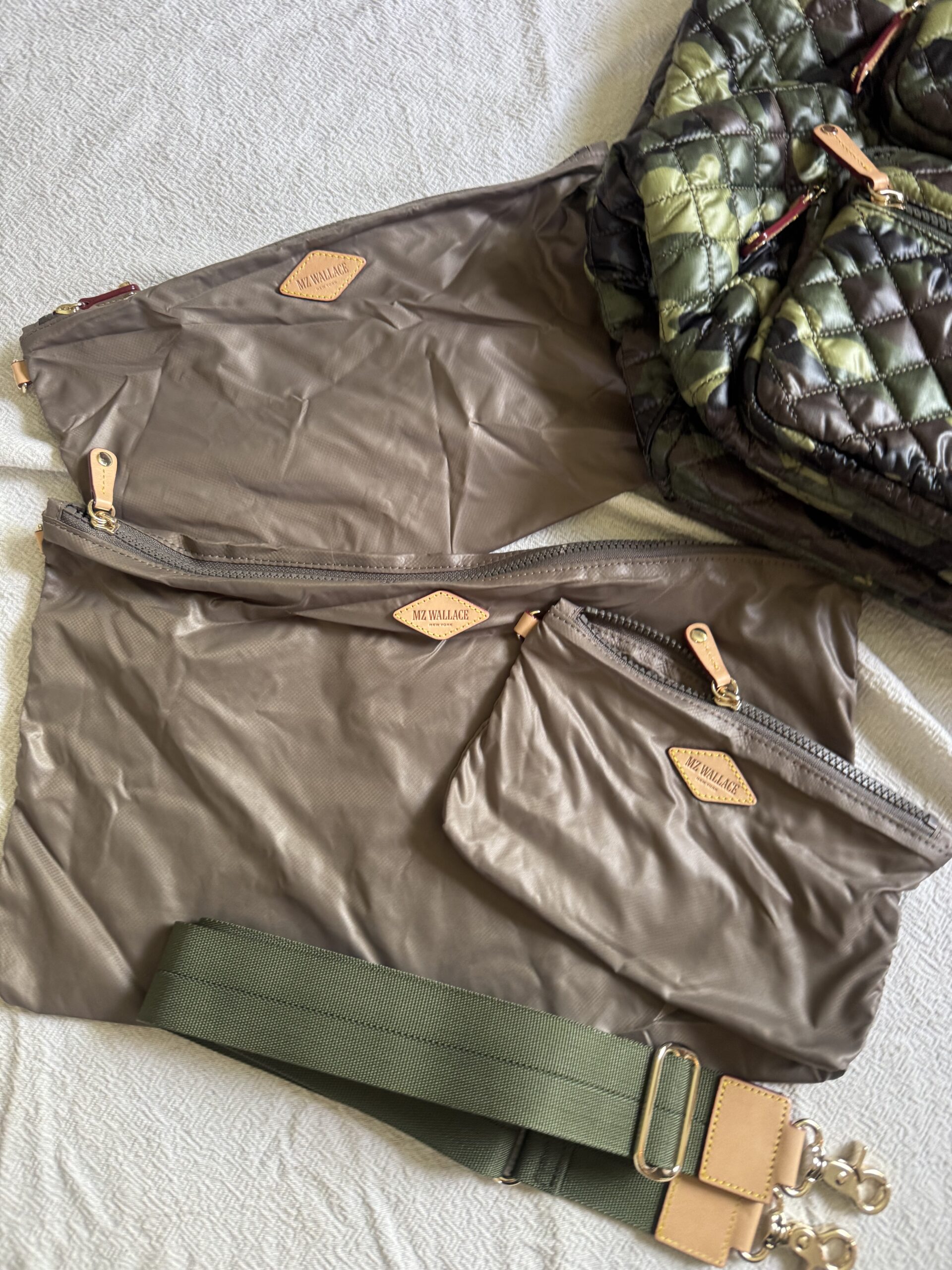 A green quilted bag with three brown zippered pouches labeled "MZ WALLACE" and a detachable green strap with gold clasps, shown on a light textured surface.