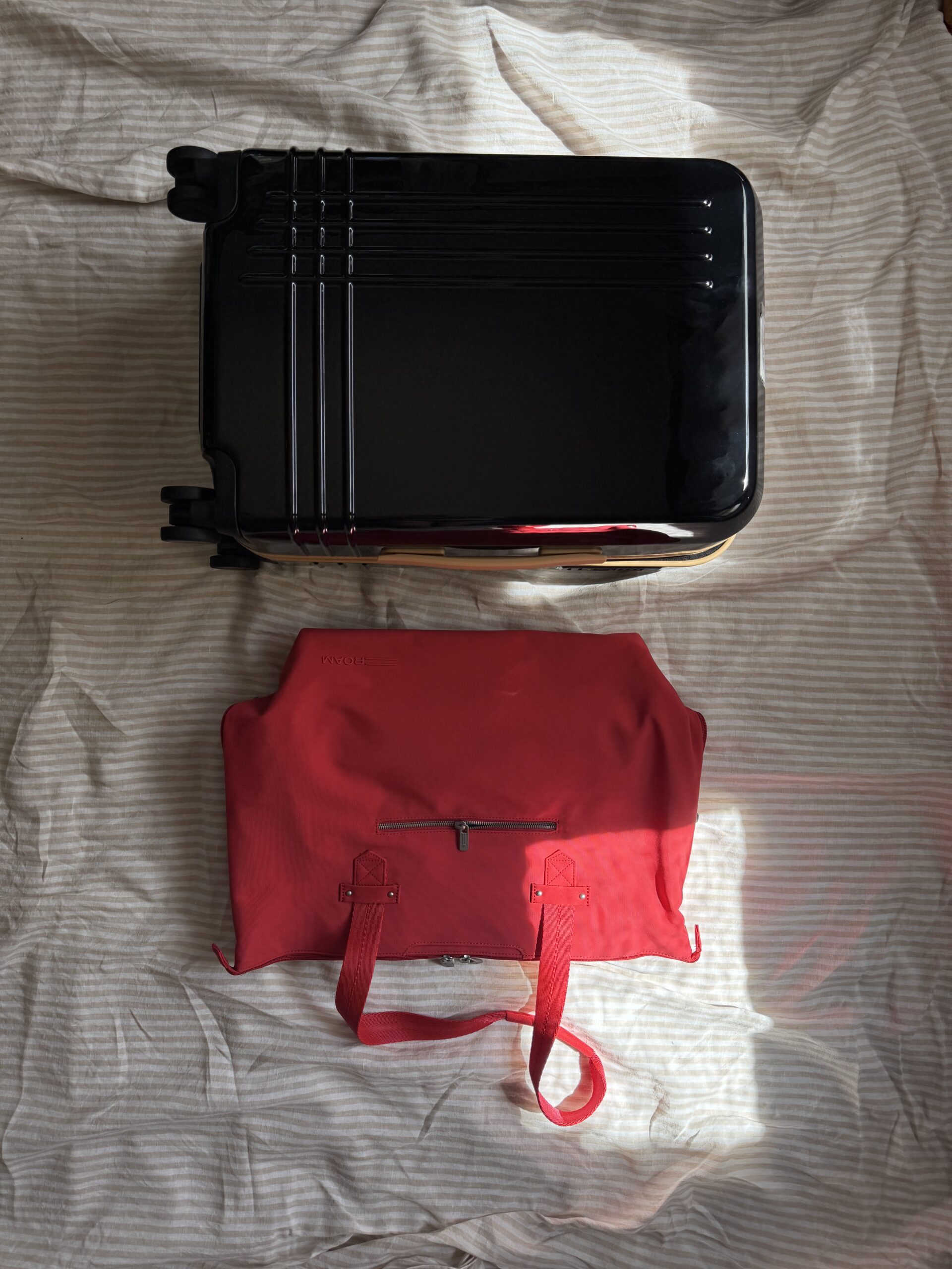 A black hard-shell suitcase and a red duffel bag are placed side by side on a beige striped fabric background.