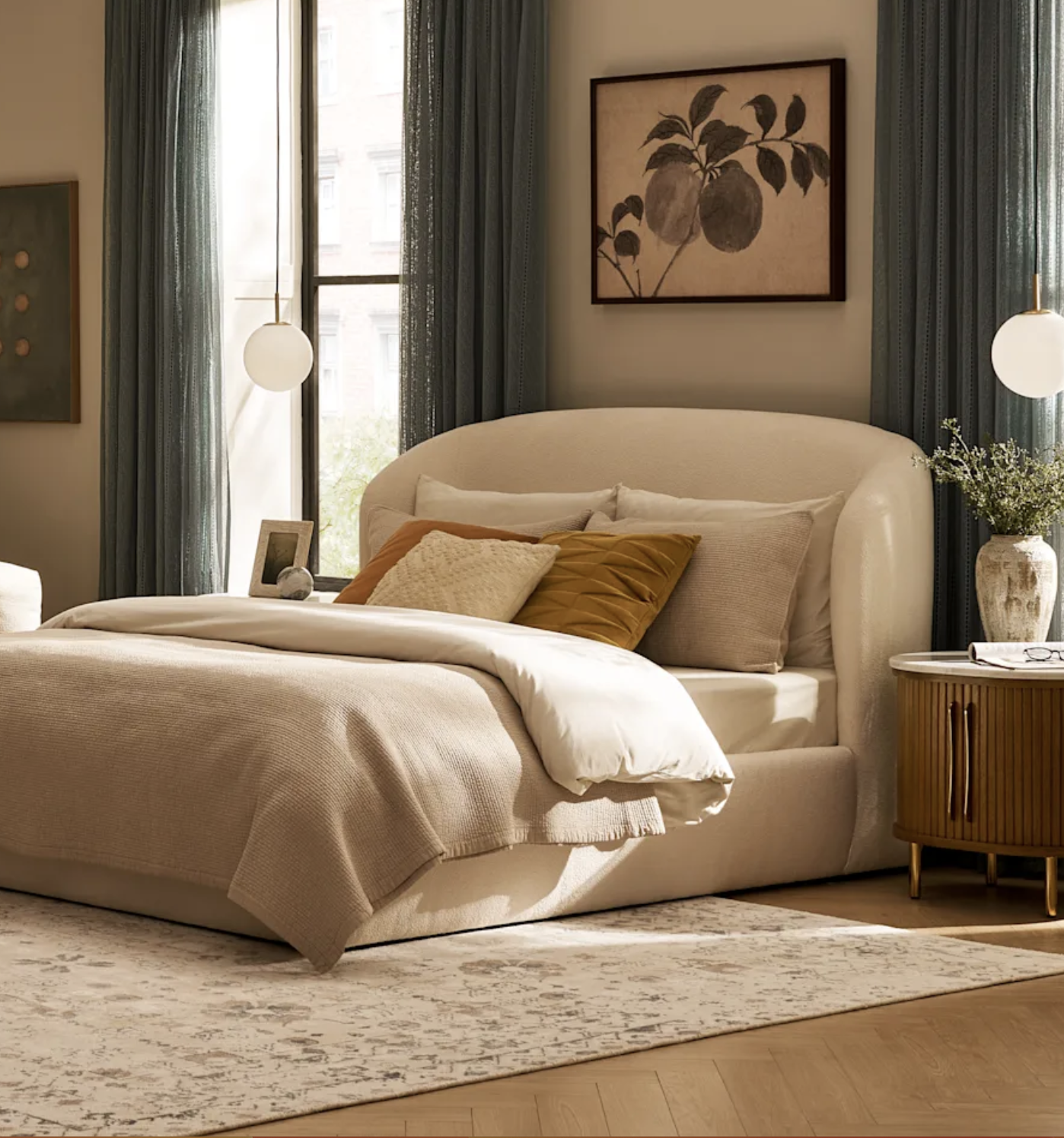 A neatly made bed with neutral bedding, accent pillows, and a curved headboard sits in a sunlit bedroom with large windows, curtains, and modern decor.