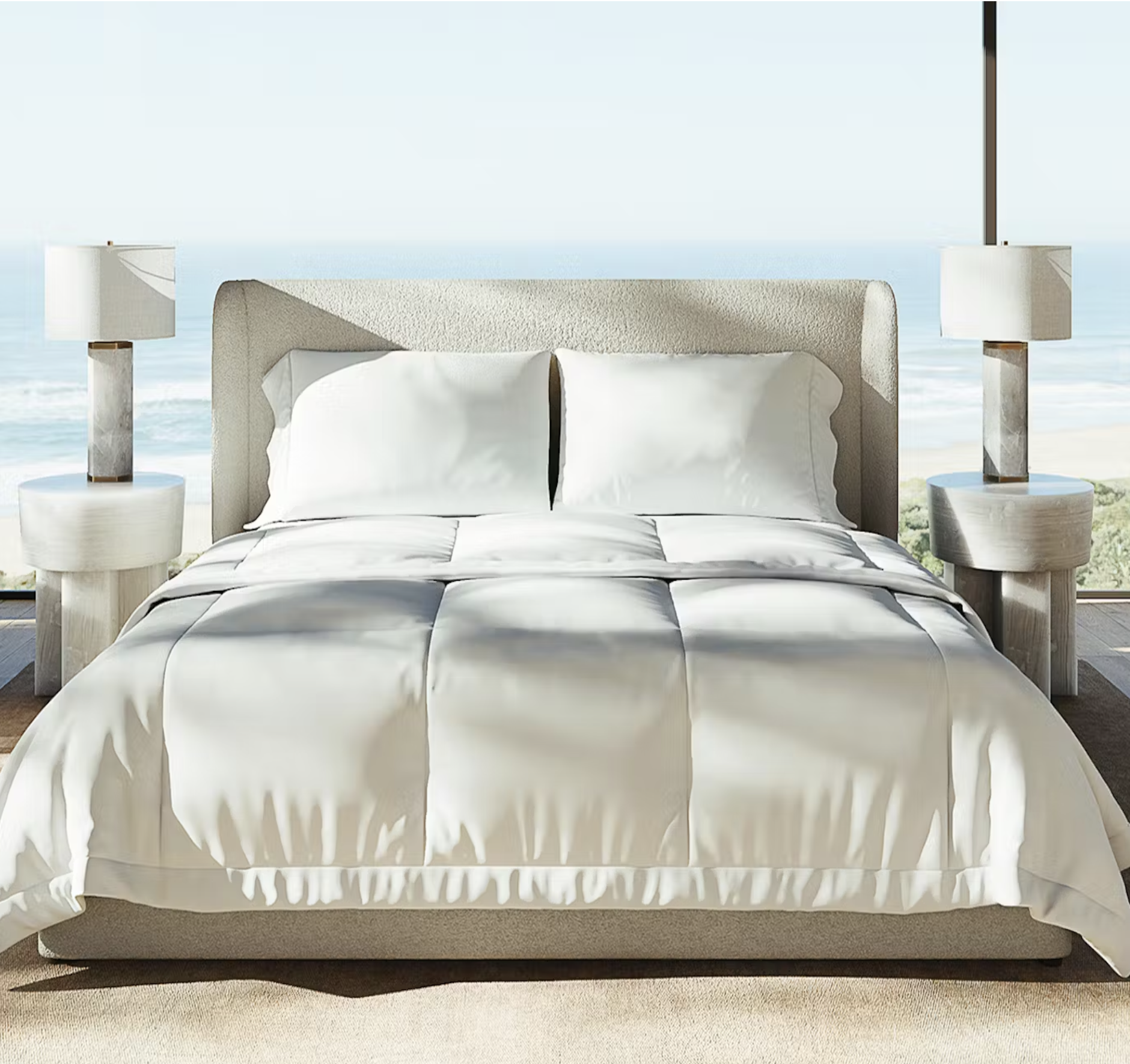 A neatly made bed with white bedding is positioned between two modern bedside tables with lamps, set in a room with large windows overlooking the ocean.