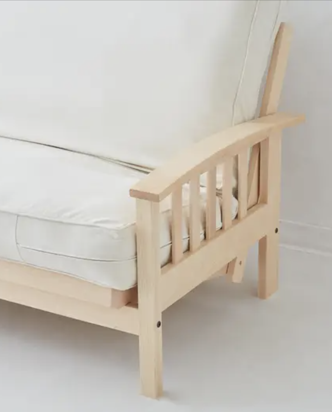 A close-up of a wooden futon frame with vertical slats on the armrest and white seat and back cushions.