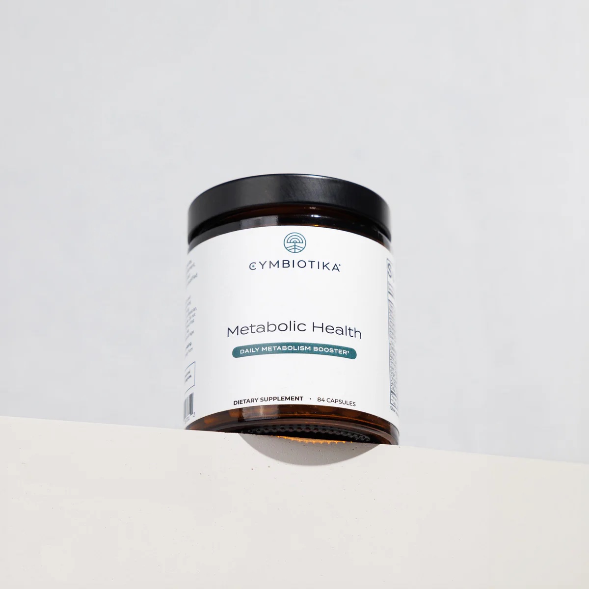 A jar of Cymbiotika Metabolic Health dietary supplement capsules is placed on a white surface against a plain background.