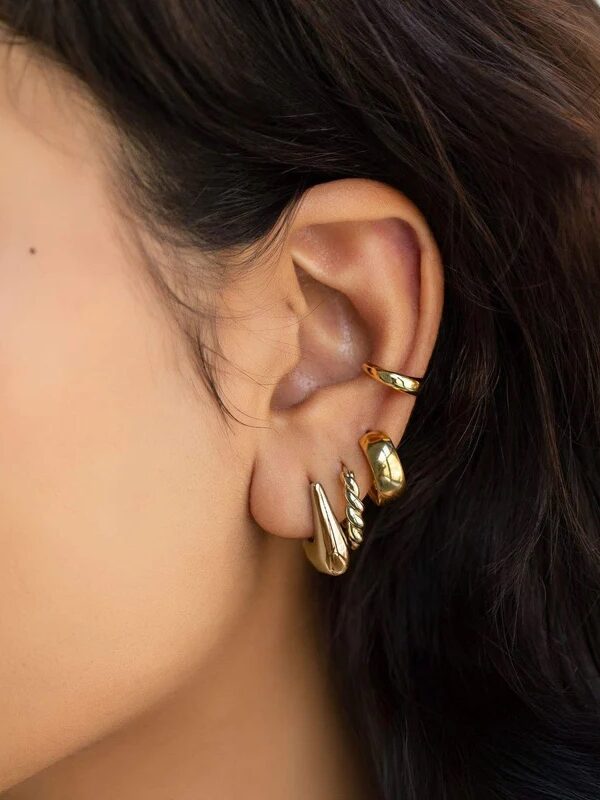 Close-up of a person's ear adorned with multiple gold hoop and cuff earrings against a background of dark, wavy hair.