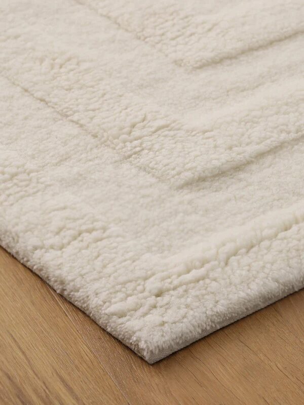 A close-up of a cream-colored, textured area rug with a raised pattern, placed on a wooden floor.