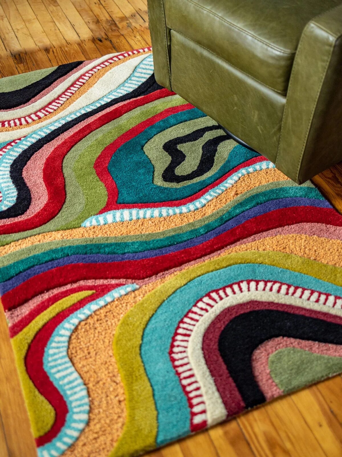 Colorful area rug with abstract wavy patterns and a green armchair positioned on a wooden floor.