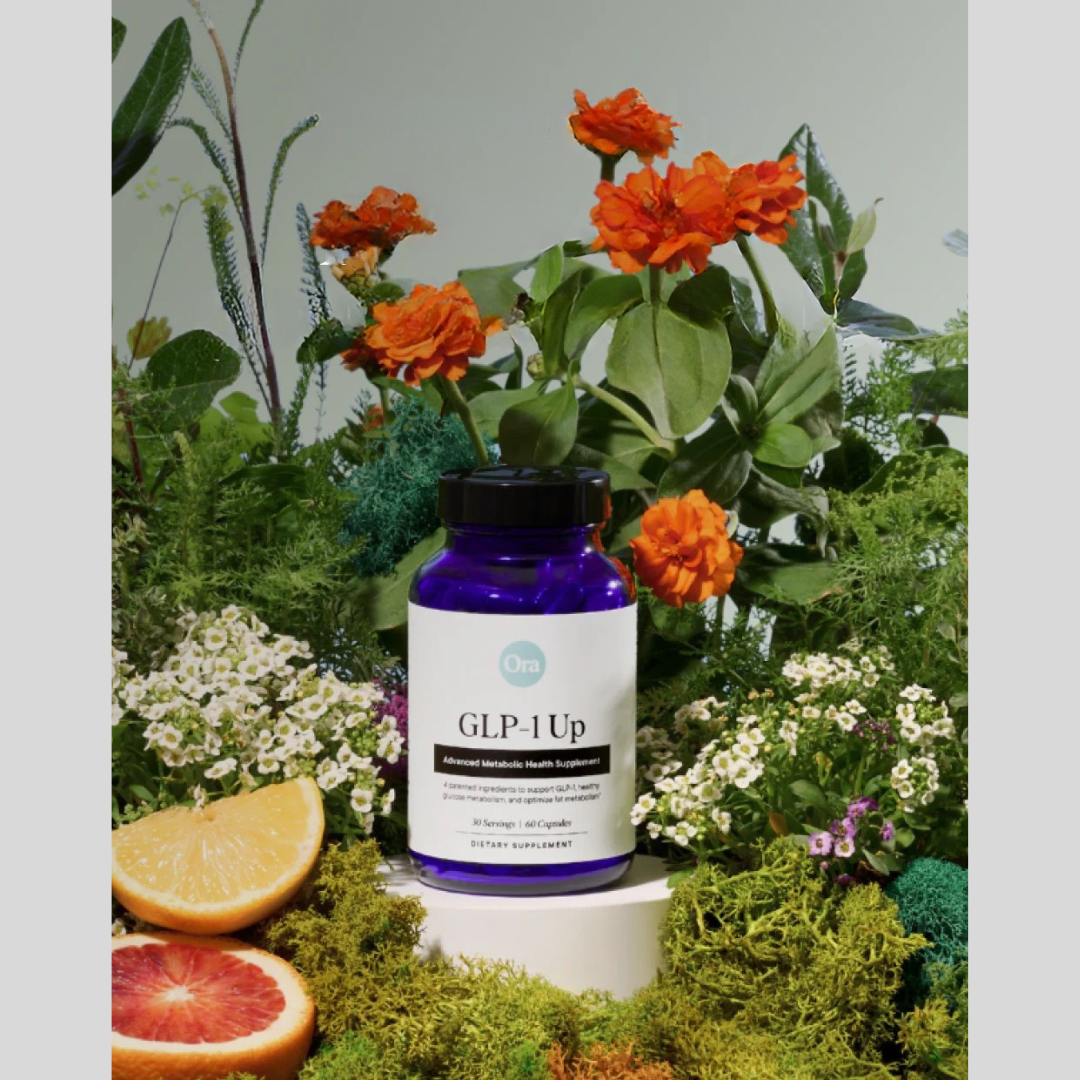 A bottle of Ora GLP-1 Up supplement sits on moss surrounded by orange flowers, greenery, and sliced citrus fruit.