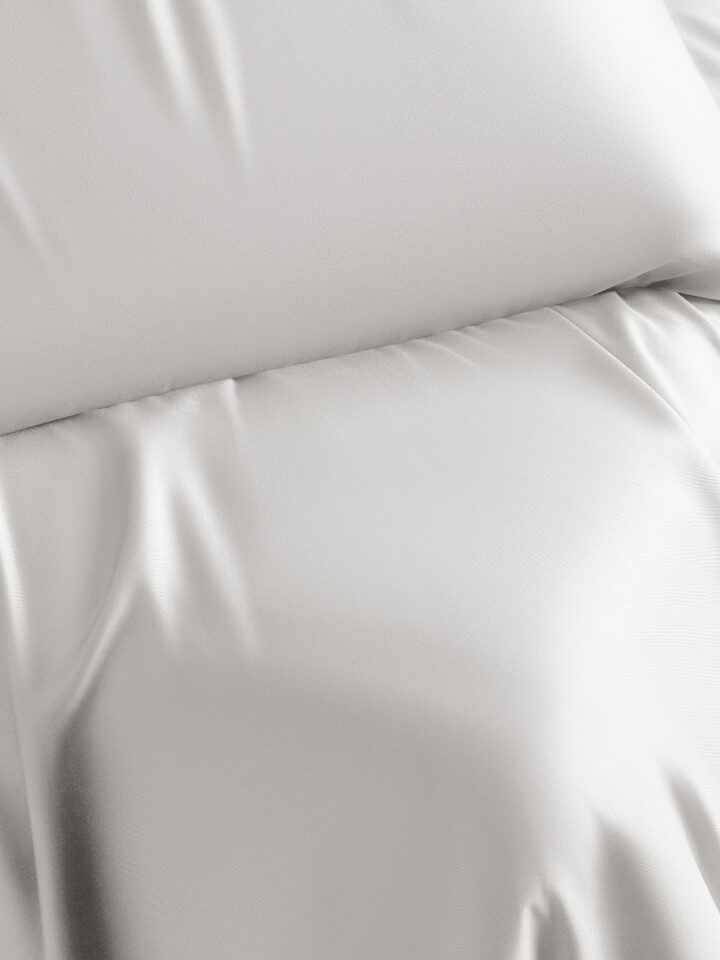 A close-up view of white bedsheets and a white pillow, both smooth and slightly wrinkled.
