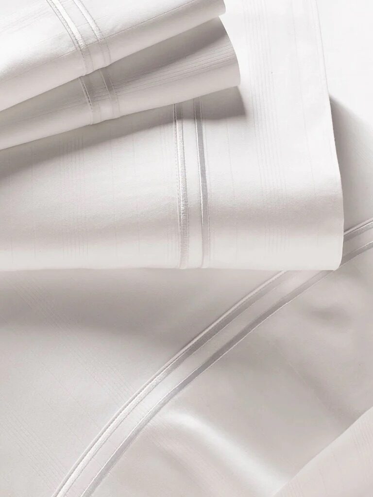 Close-up of folded white bed sheets with subtle striped patterns and stitched borders.