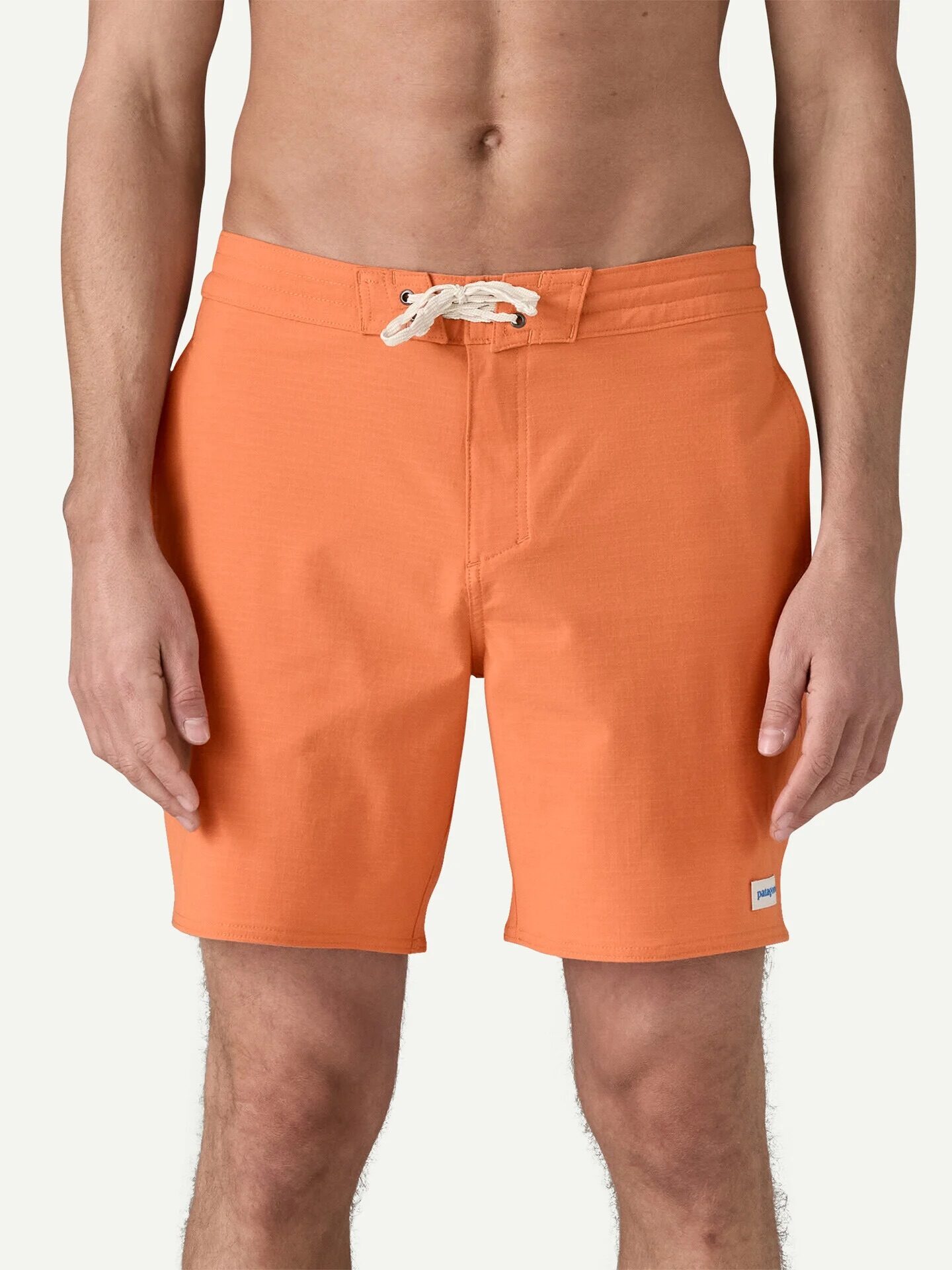A person wearing orange swim trunks with a white drawstring, standing against a plain light background.