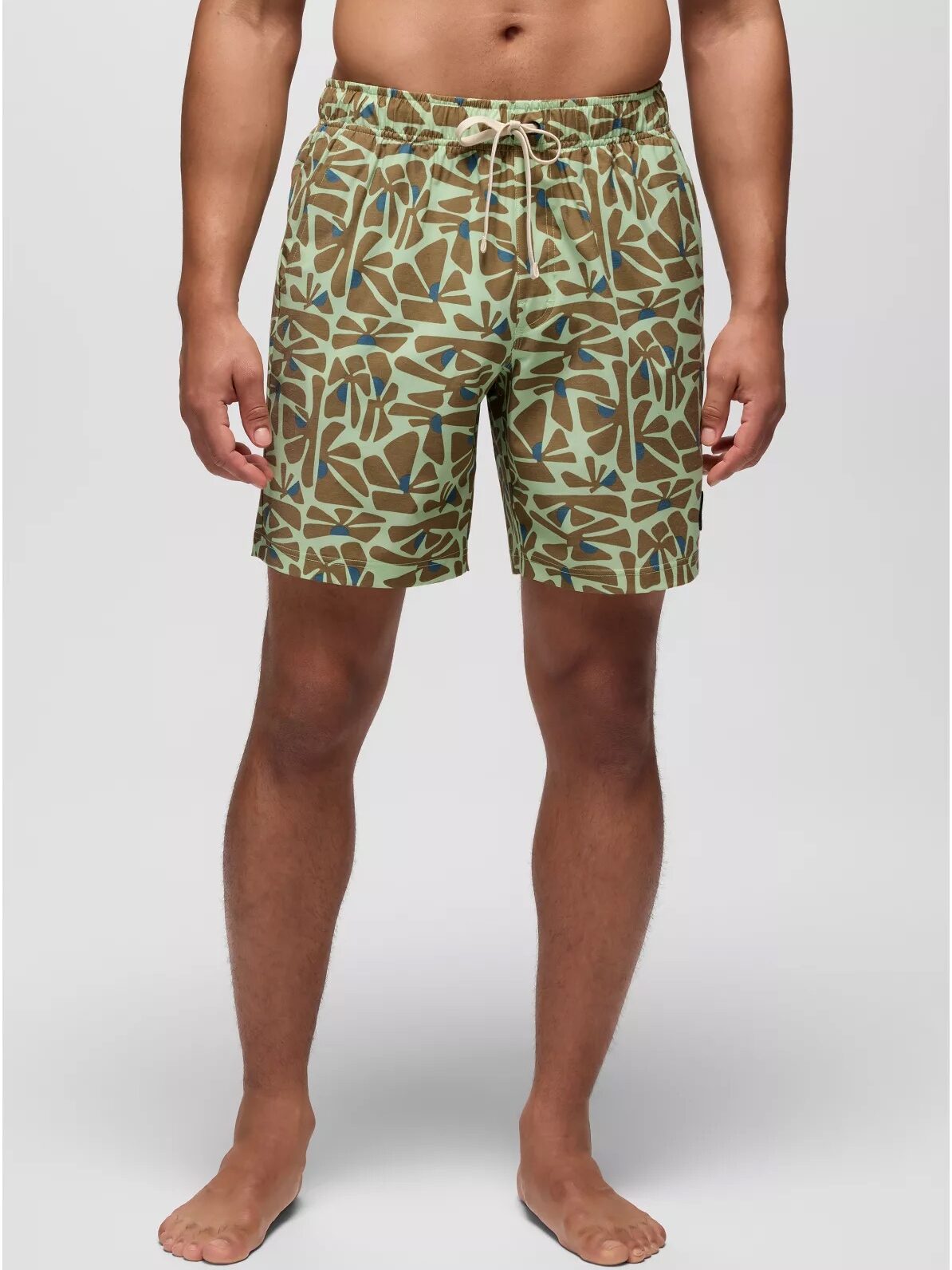 A person wearing green and brown patterned swim trunks, standing barefoot against a plain light background.