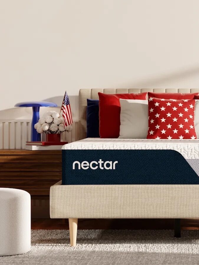 A neatly made bed with a Nectar mattress and red, white, and blue patriotic-themed pillows, set in a modern bedroom with American flag decorations.