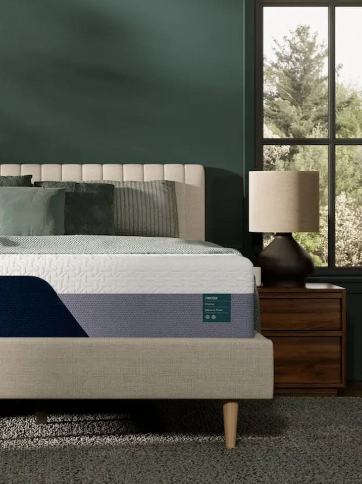 A neatly made bed with a Nectar mattress in a modern bedroom featuring two wooden nightstands, matching lamps, and large windows with outdoor views.