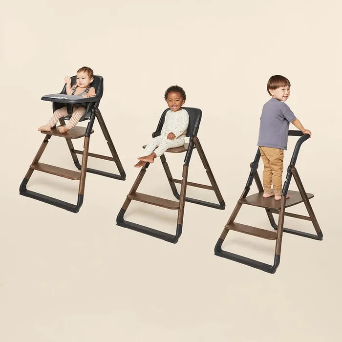 Three young children sit or stand on adjustable high chairs with wooden frames and dark seats, each demonstrating different seating positions.