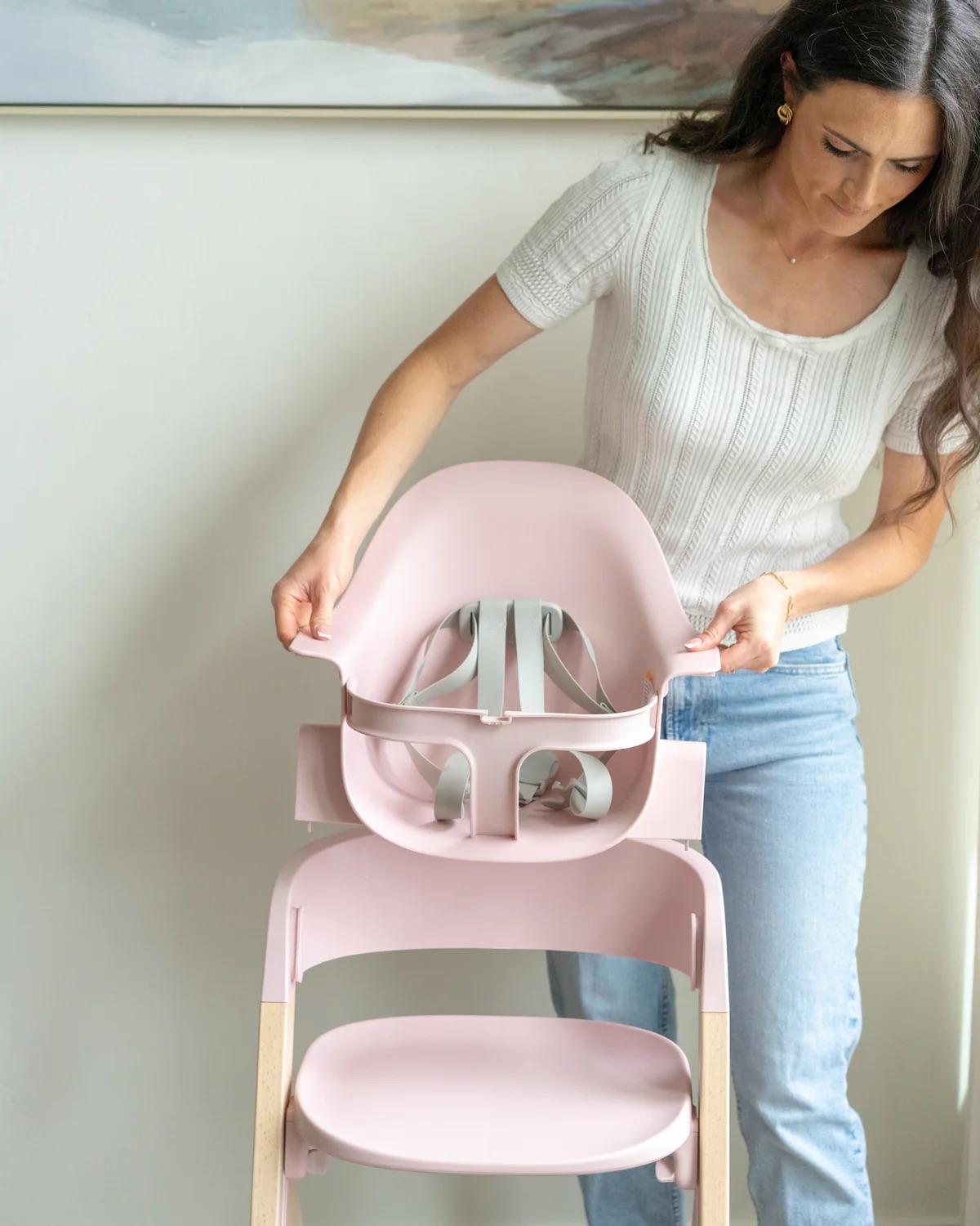 A woman assembles a pink high chair by attaching the seat component to the base frame in a well-lit room.