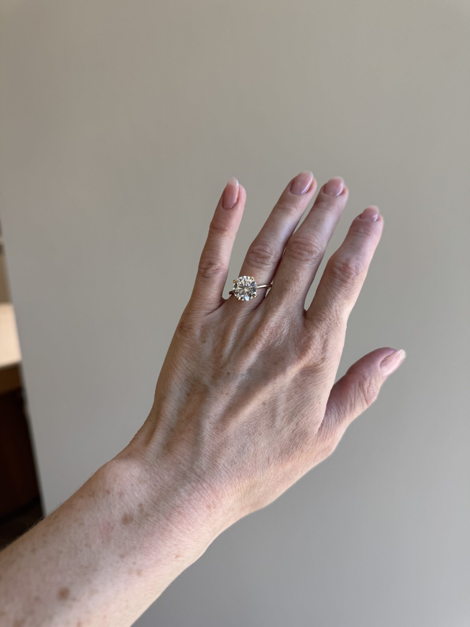 A hand with light skin and short, natural nails is shown wearing a silver ring with a large, round, clear gemstone.