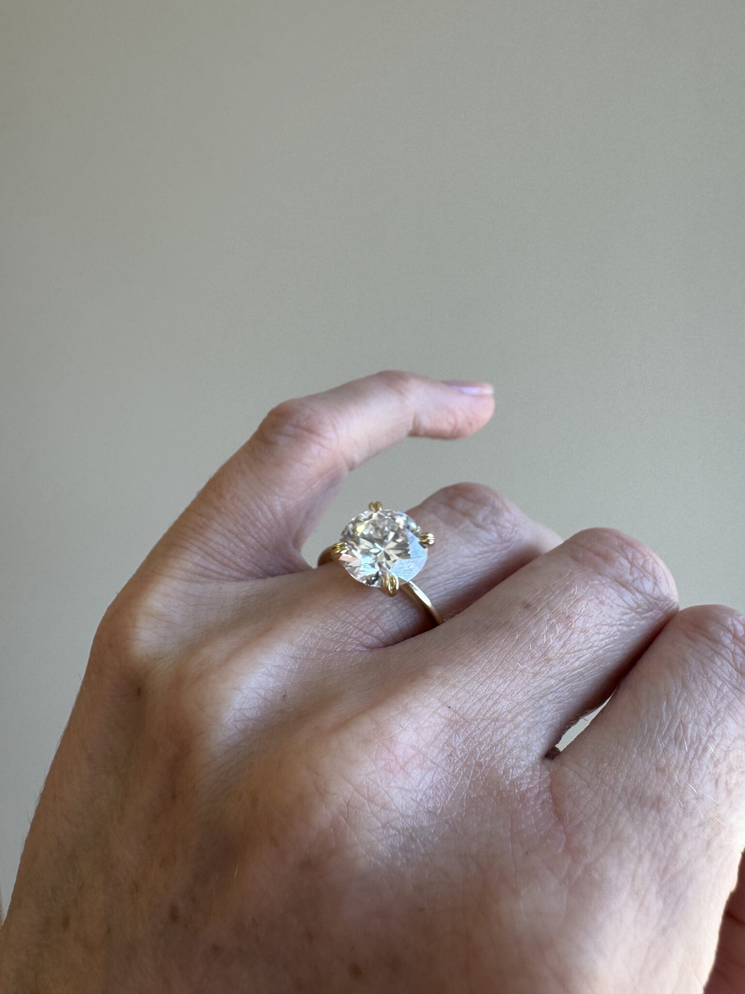 A hand wearing a gold ring with a large, round, clear gemstone set in a prong setting.