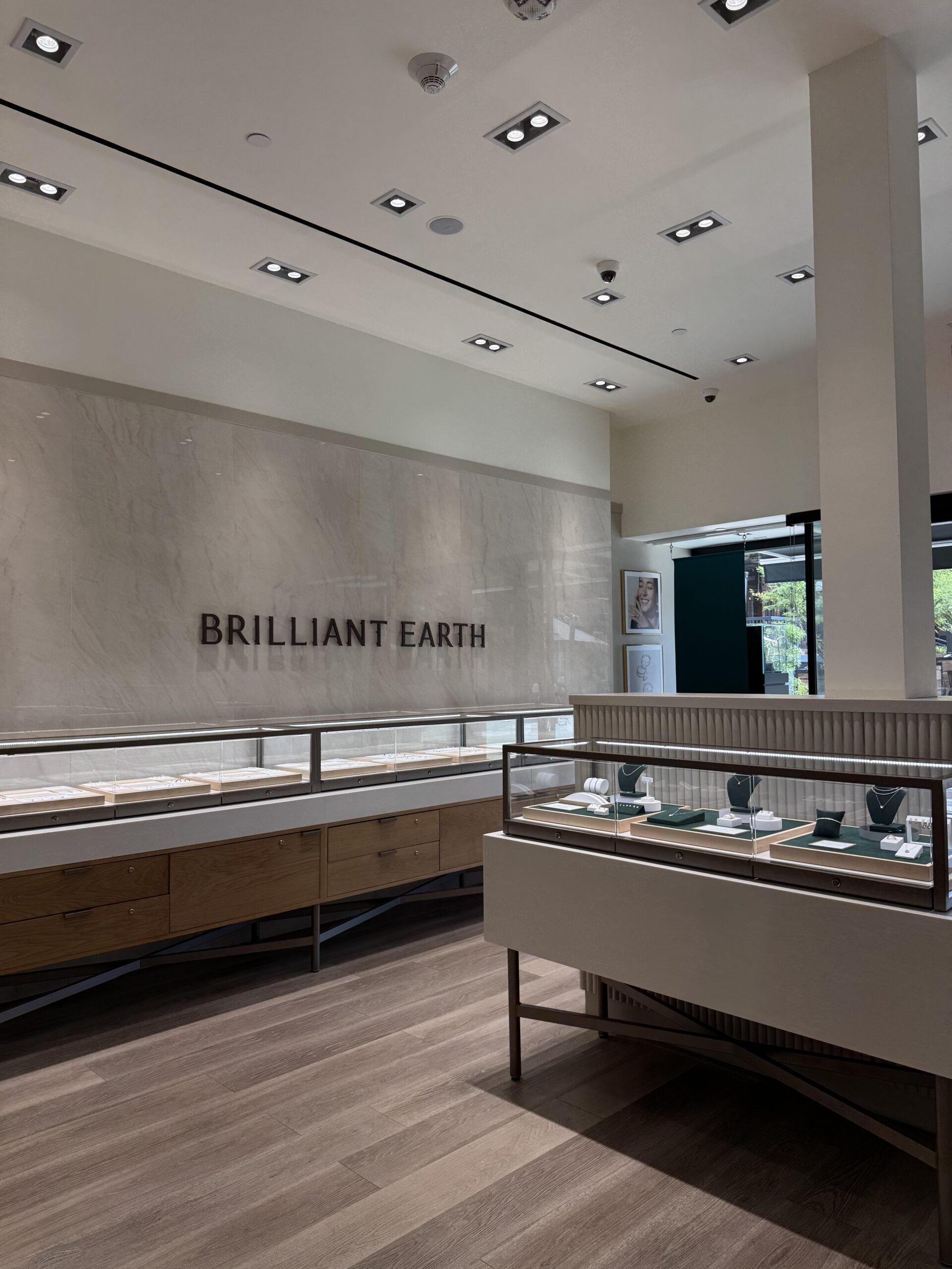 Interior of a Brilliant Earth jewelry store with display cases containing jewelry items on a wooden floor, and large signage on the wall.