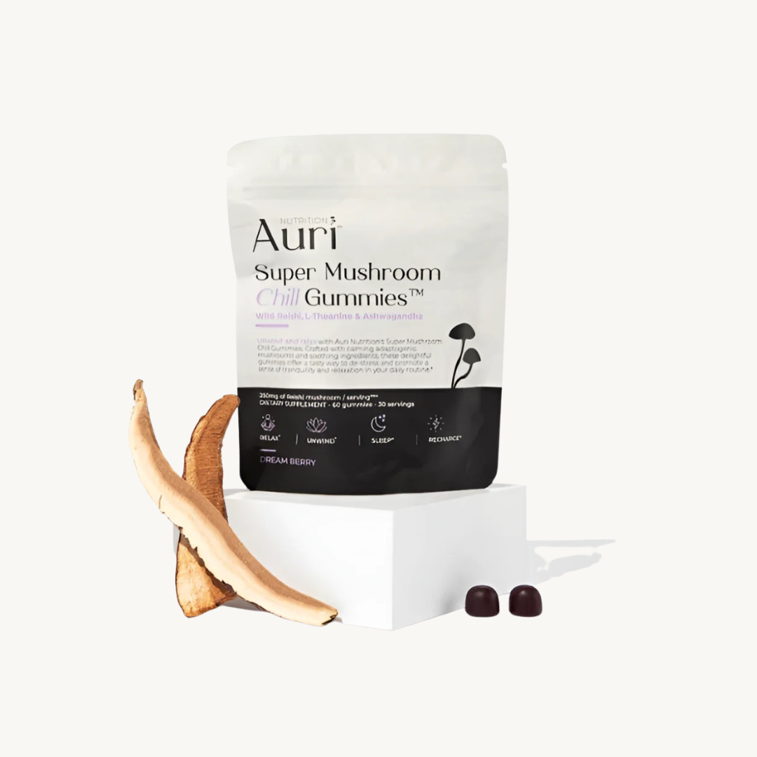A bag labeled "Auri Super Mushroom Chill Gummies" stands upright with two dark gummies and two sliced mushroom pieces on a white block against a plain background.