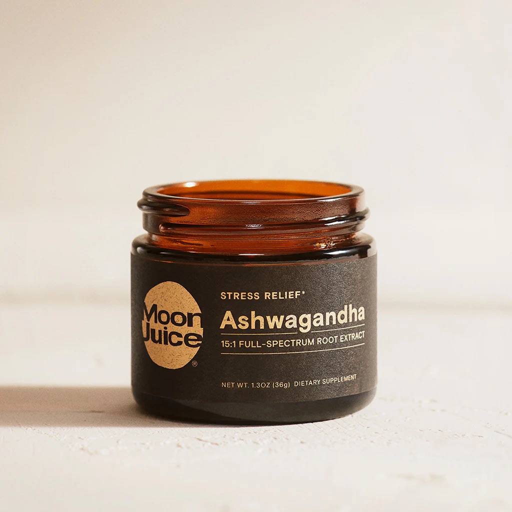 An open amber glass jar labeled "Moon Juice Ashwagandha 15:1 Full-Spectrum Root Extract" sits on a pale surface.