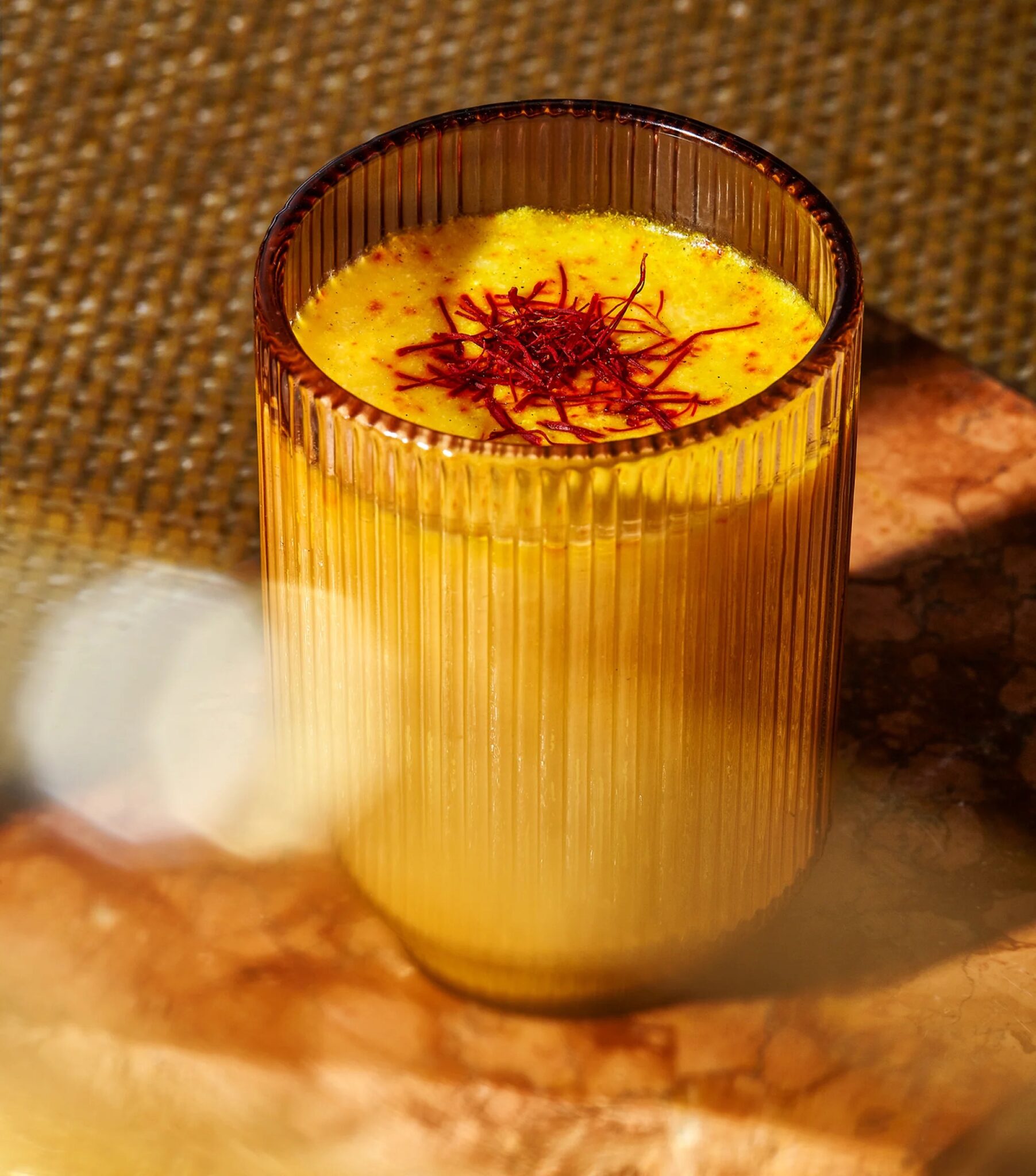 A glass of yellow turmeric milk topped with saffron strands, placed on a marble surface with textured background.