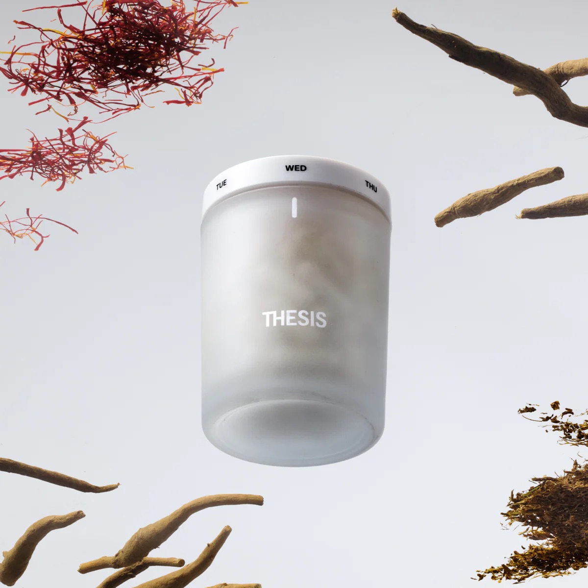 A frosted container labeled "THESIS" with a white lid marked with days of the week, surrounded by herbs and roots on a light background.