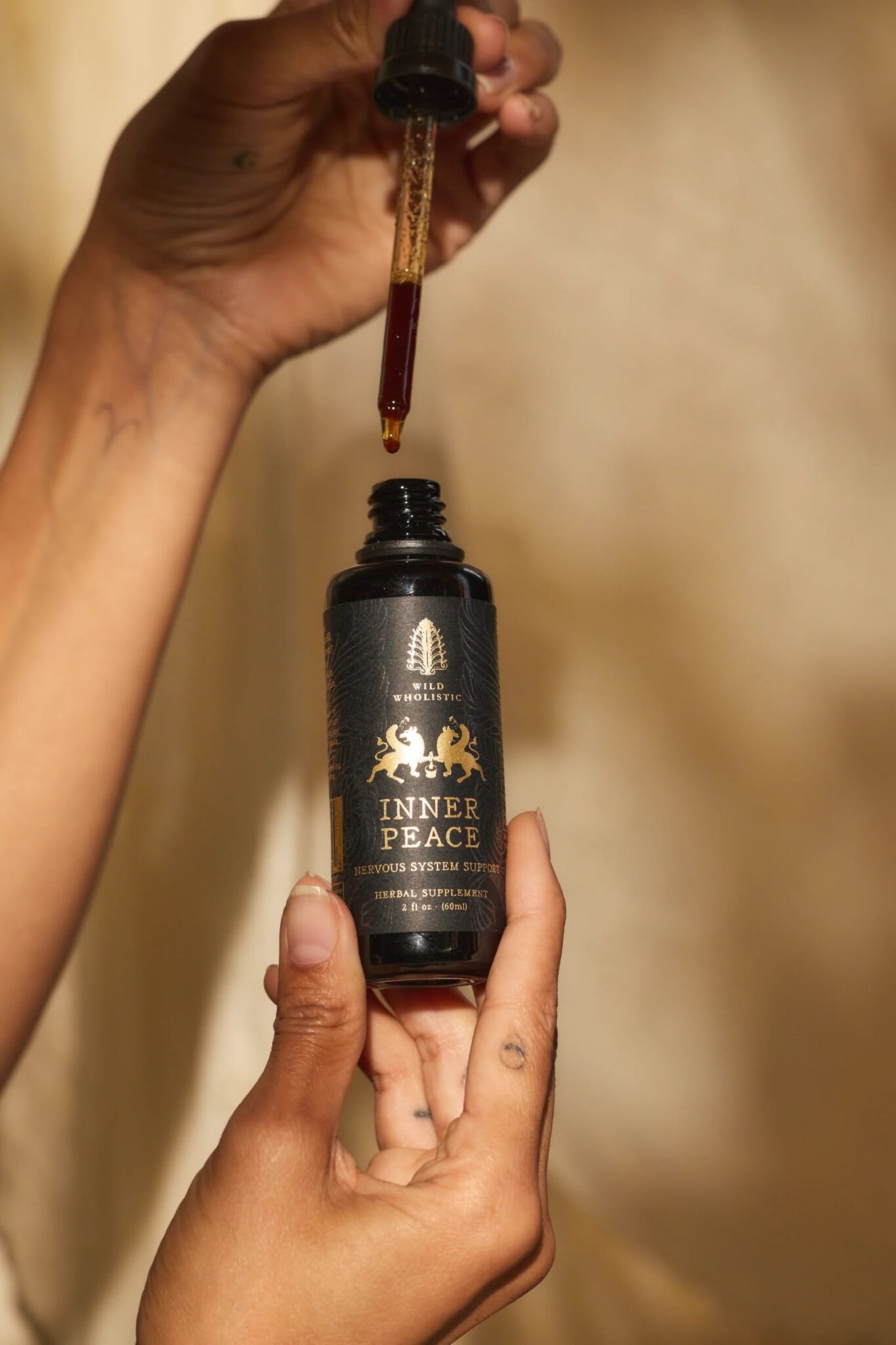 A person holds a dropper bottle labeled "Inner Peace Nervous System Support" with a dropper of liquid held above the bottle.