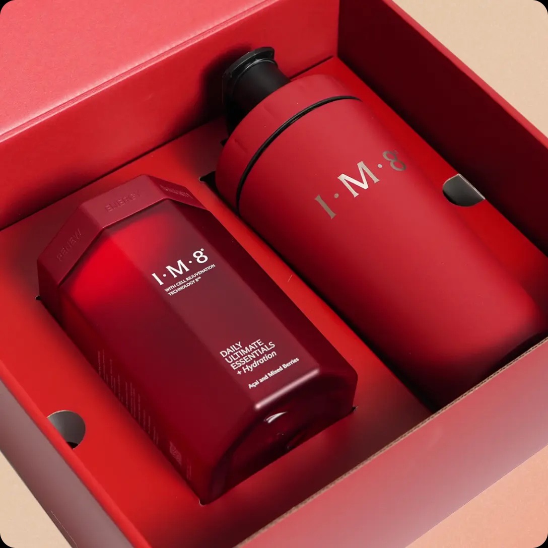 A red boxed set containing a bottle labeled I.M.8 Daily Ultimate Nutrition and a matching red tumbler with a black lid.