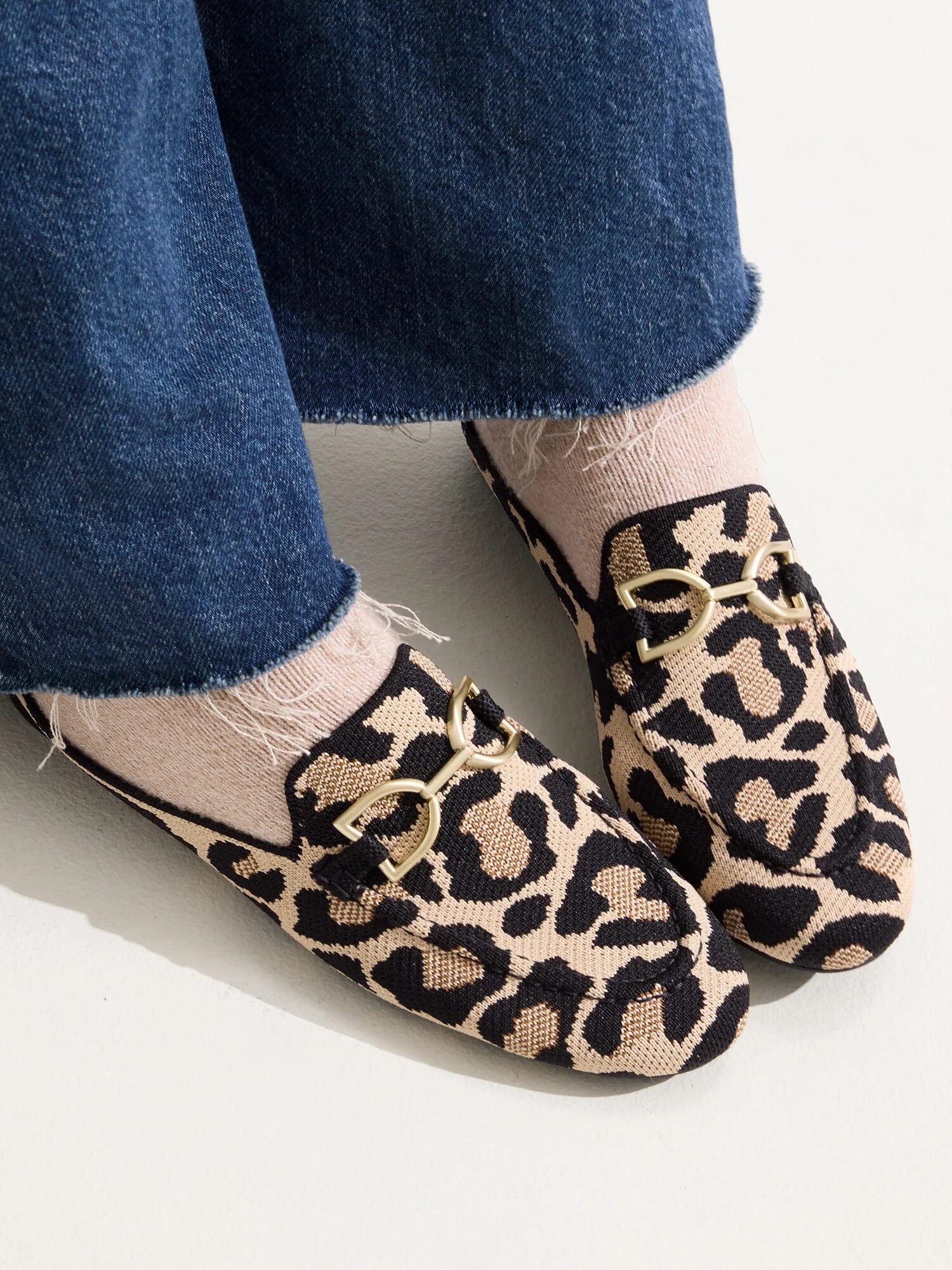 Close-up of a person wearing wide-leg blue jeans and leopard print loafers with gold buckle details.