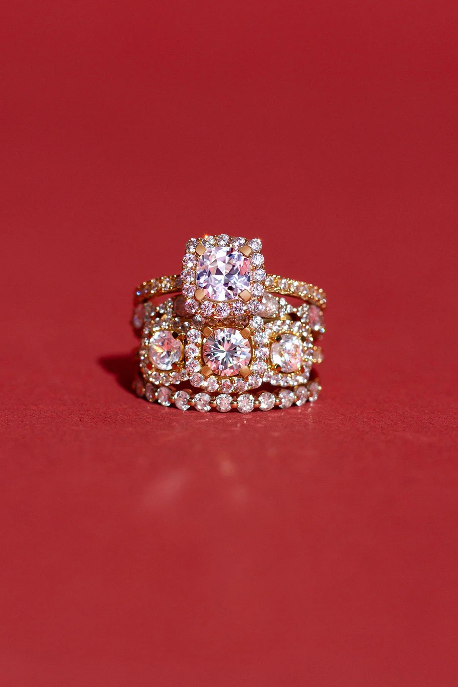 Three gold rings with diamond settings are stacked together against a solid red background.