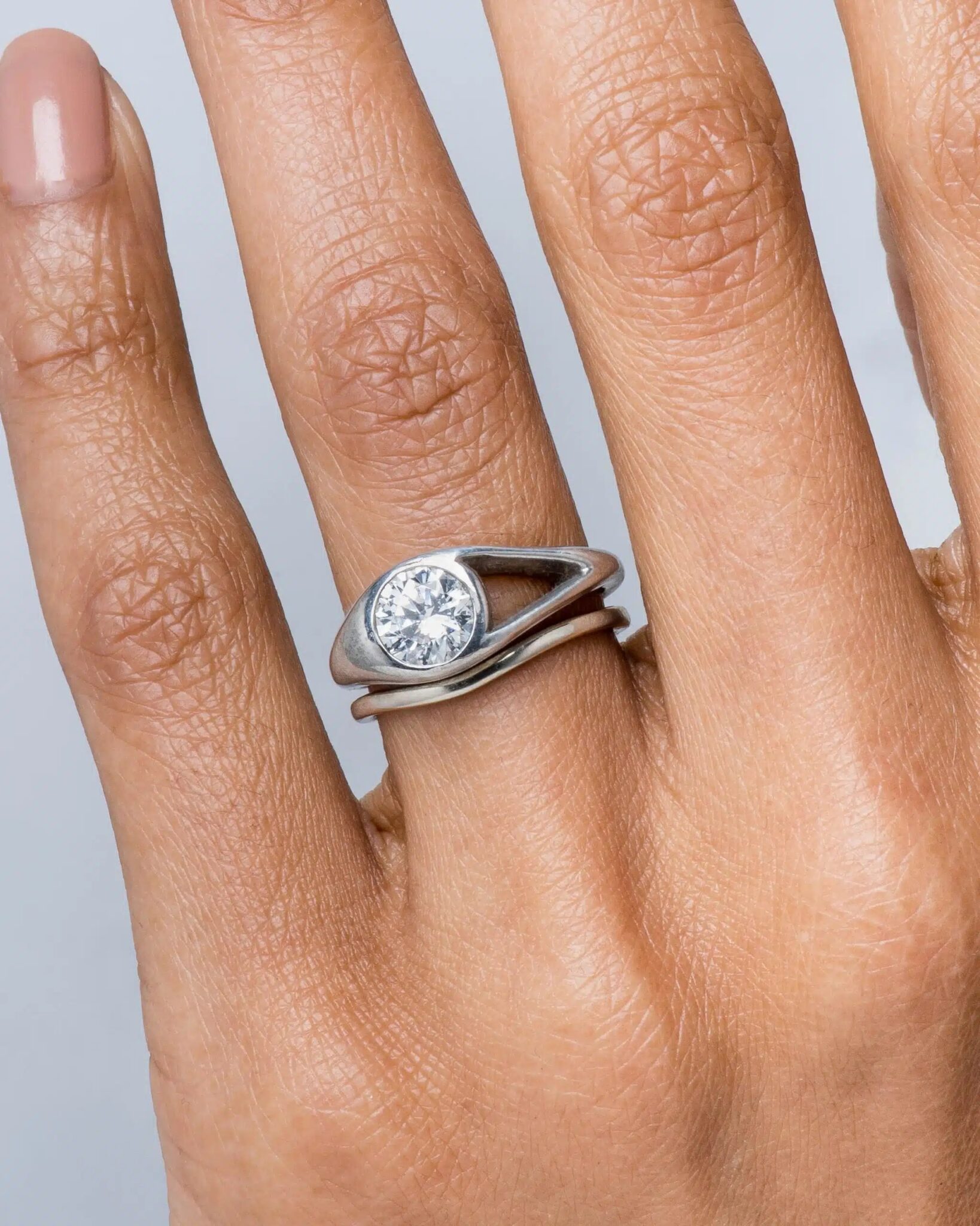 A hand wearing a silver ring with a round, clear gemstone set in a modern, open design.