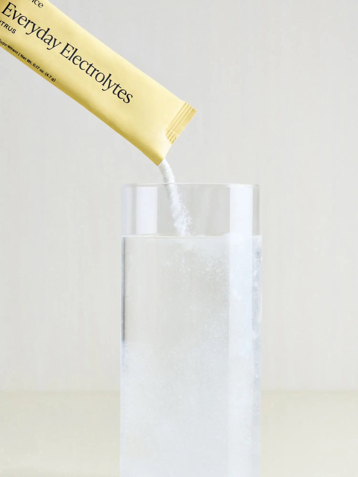 A packet labeled "Everyday Electrolytes" is being poured into a clear glass of water.