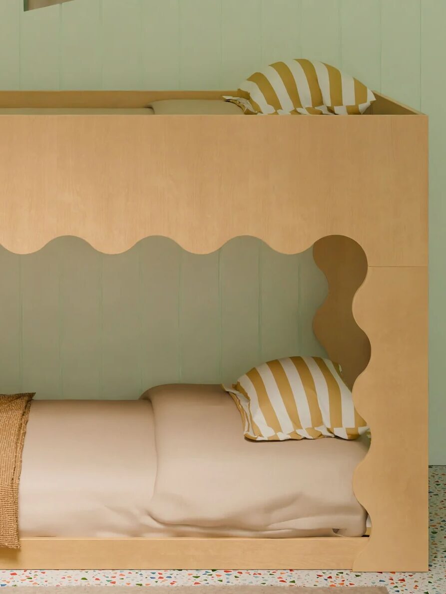 A wooden bunk bed with wavy-cut openings, striped pillows, and neutral bedding is set against a pale green wall with patterned flooring.