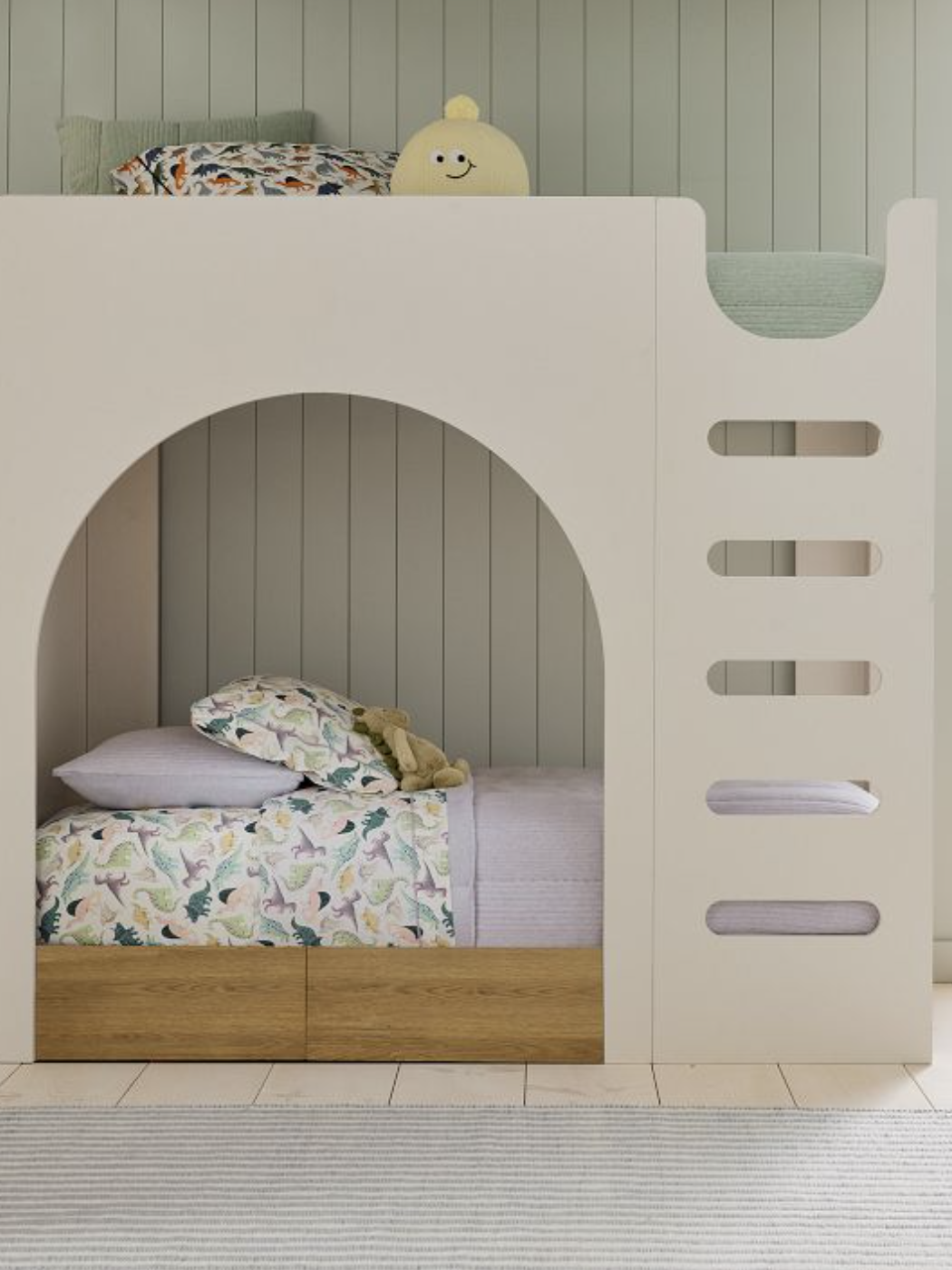 Modern bunk bed with wooden drawers, patterned bedding, a plush toy on each bed, and a built-in ladder, set against a vertical panel wall.