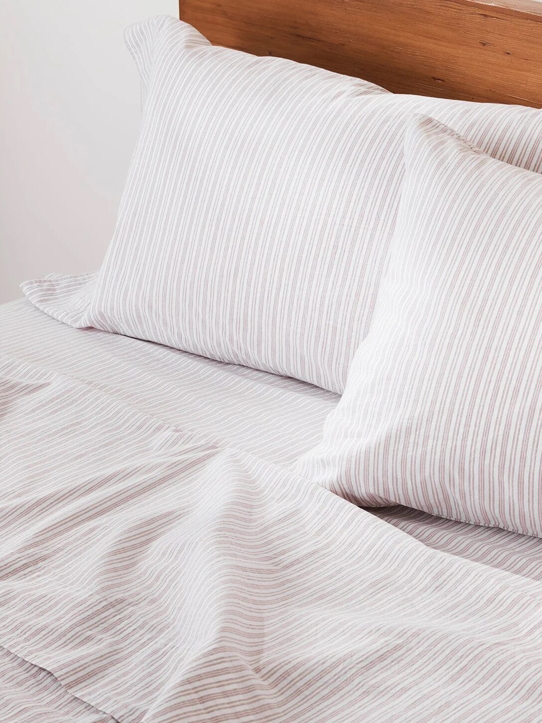 Two white pillows with light gray stripes rest against a wooden headboard on a bed with matching striped sheets and a slightly rumpled blanket.
