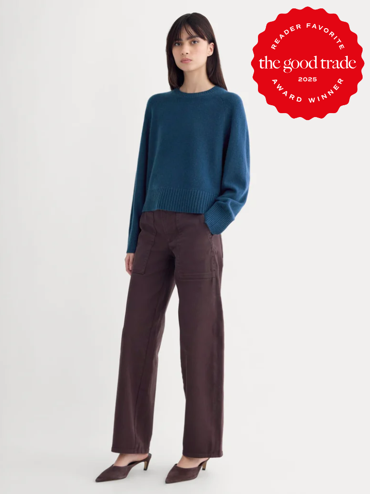 Woman wearing a teal sweater and brown wide-leg pants stands against a plain background; a red "The Good Trade 2025 Award Winner" badge appears in the upper right corner.