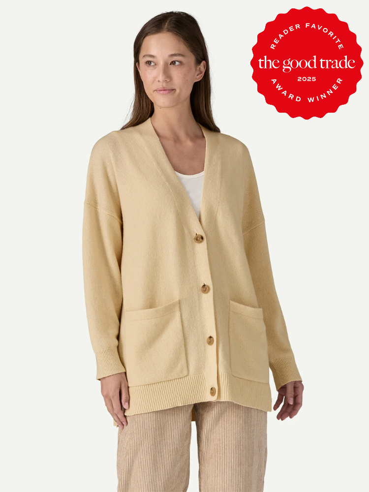 A woman wears a beige button-up cardigan with front pockets over a white top and beige pants. A red badge reads “the good trade award winner 2025.”.