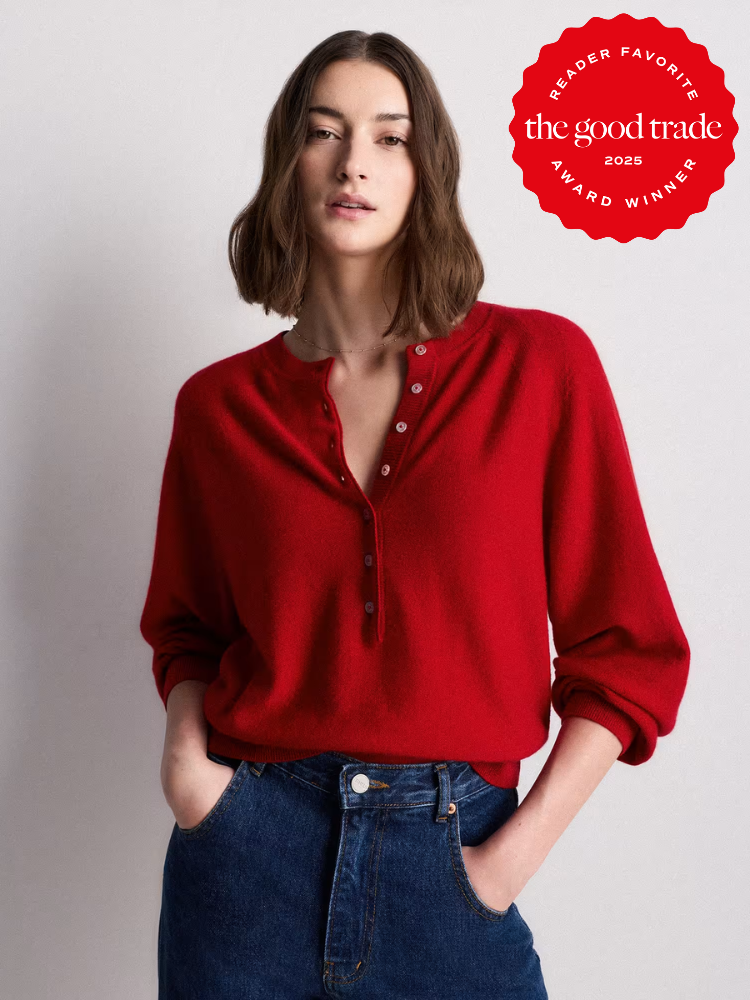 A woman wearing a red henley sweater and blue jeans stands against a plain background. A red badge in the corner reads "The Good Trade 2025 Reader Favorite Award Winner.