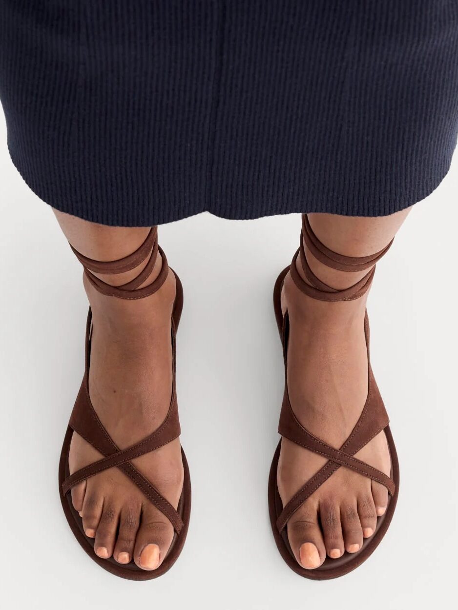 A person wearing brown strappy sandals and a navy blue skirt, viewed from above.