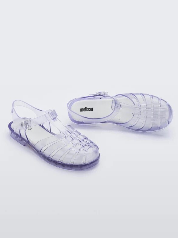 A pair of transparent purple jelly sandals with woven straps and ankle buckles, displayed on a light background. The insole is labeled "melissa.
