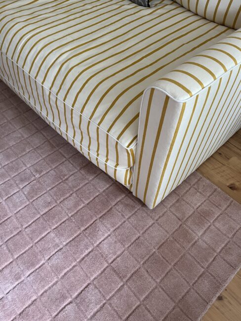 A yellow and white striped sofa is positioned next to a light pink checkered rug on a wooden floor.