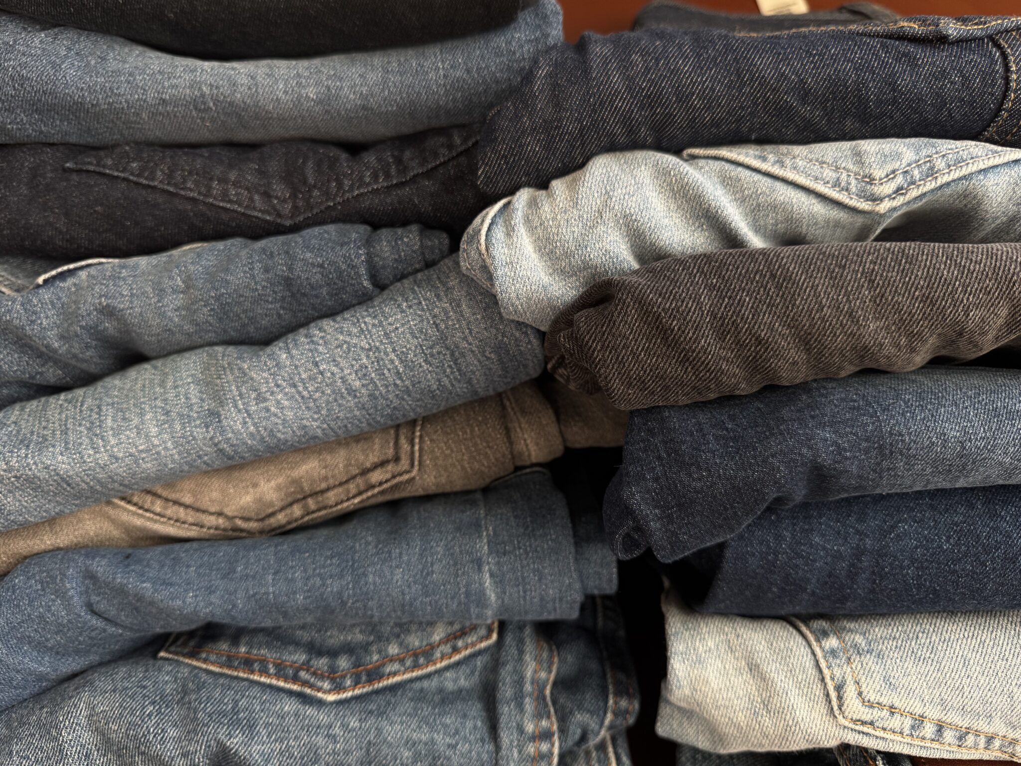 A stack of folded denim jeans and pants in various shades of blue and black.