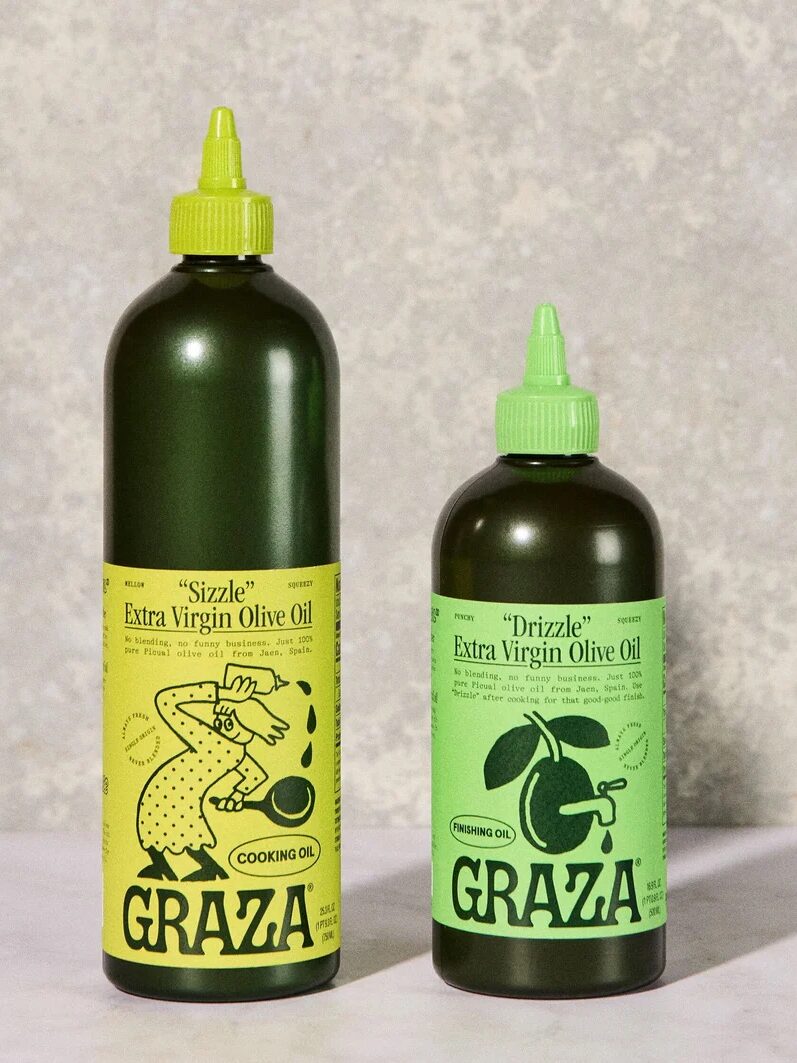 Two green bottles of Graza extra virgin olive oil, labeled "Sizzle" for cooking and "Drizzle" for finishing, are placed side by side on a light surface.