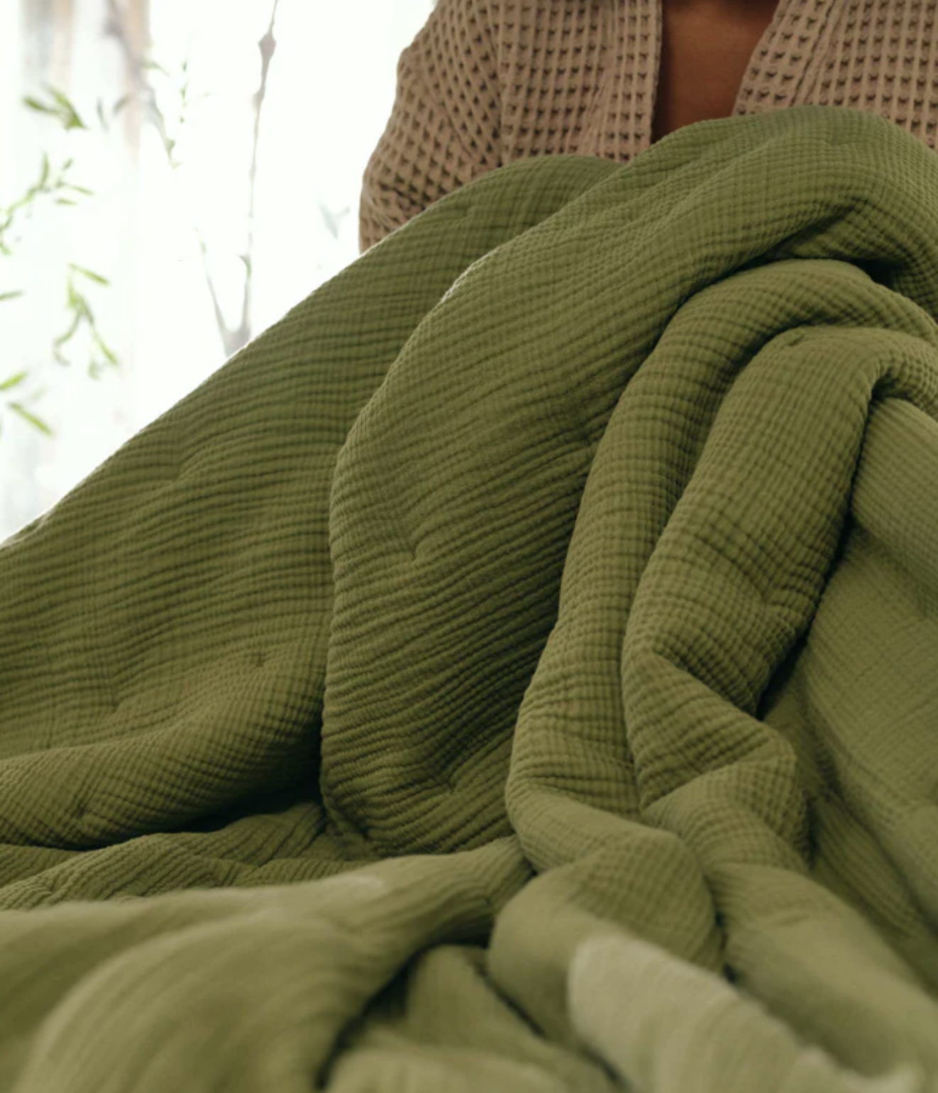 A person holding or arranging a large, textured green blanket or comforter, with part of their upper body visible.