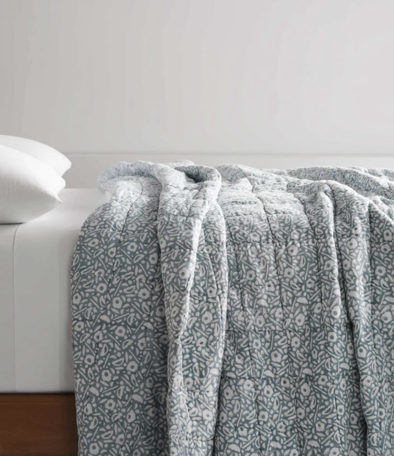 A neatly made bed with a white pillow and a blue and white patterned quilt draped over the edge.