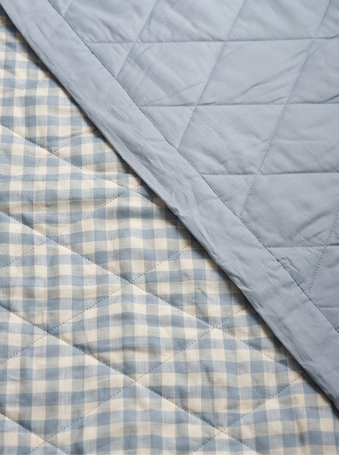 Close-up of a quilt with one side featuring a solid light blue fabric and the other side displaying a blue and white checkered pattern, both stitched in a diamond pattern.