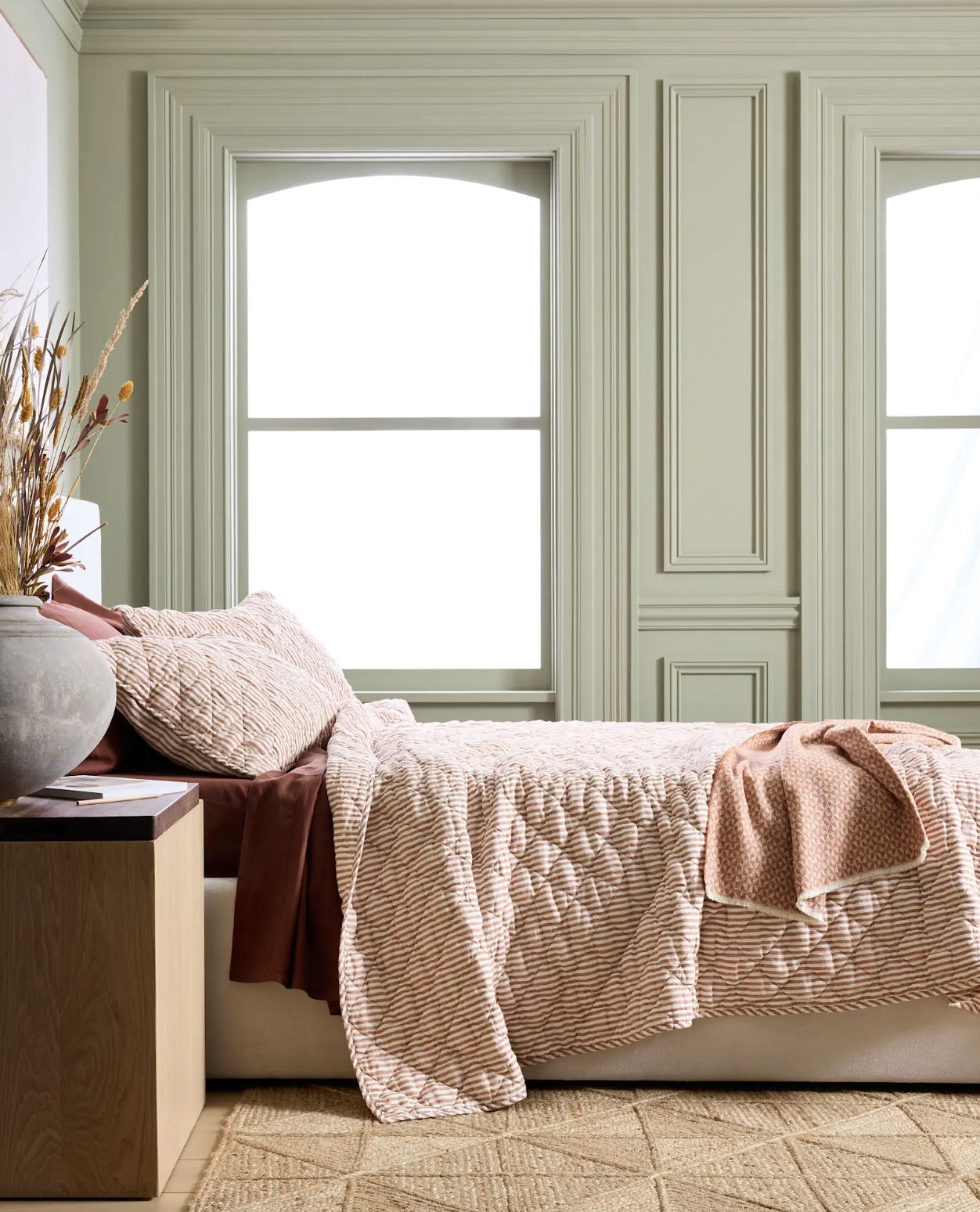 A bed with a vase of dried flowers.