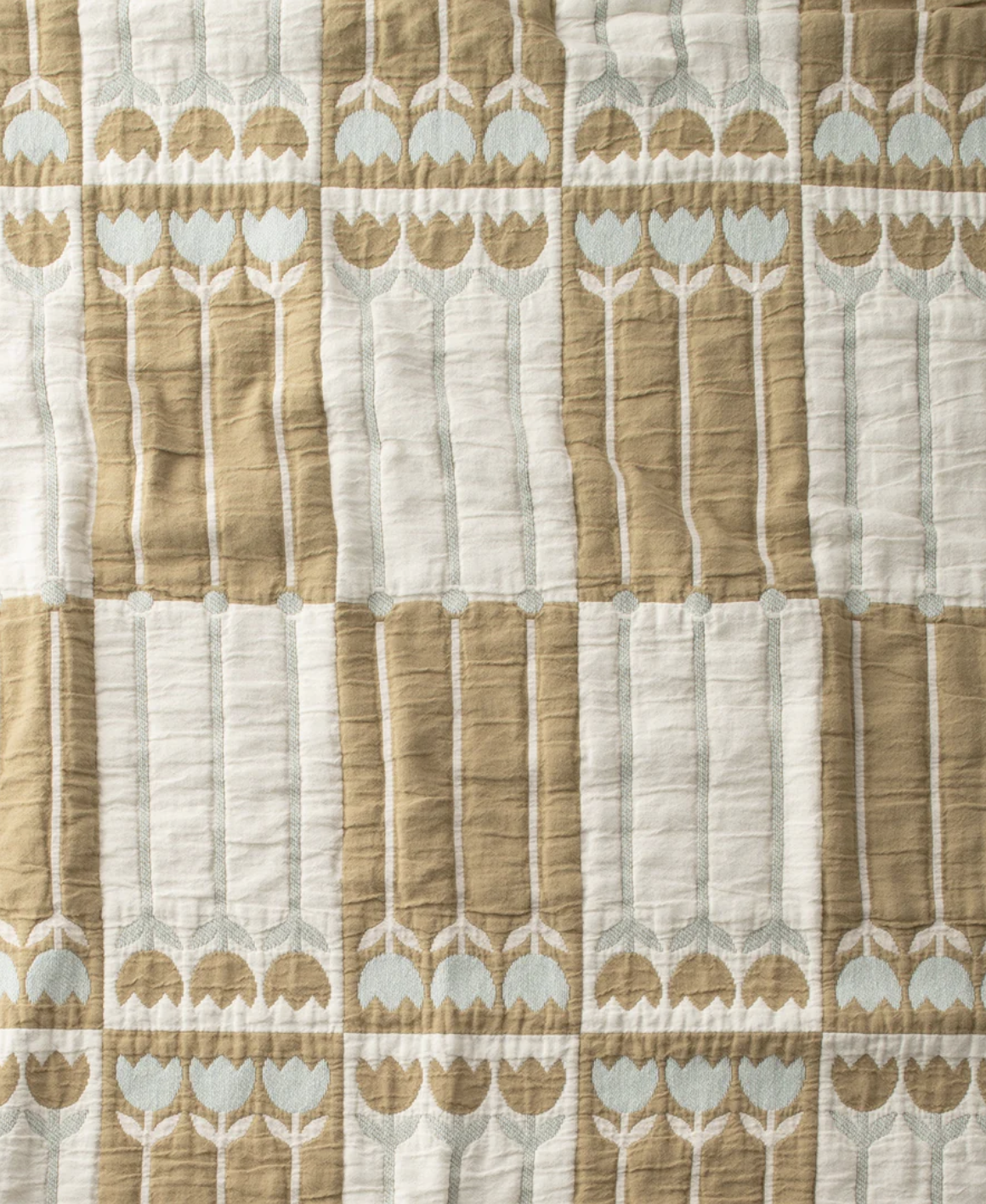 Quilted fabric with a repeating geometric pattern of stylized tulips in light brown and white, arranged in vertical columns and horizontal rows.