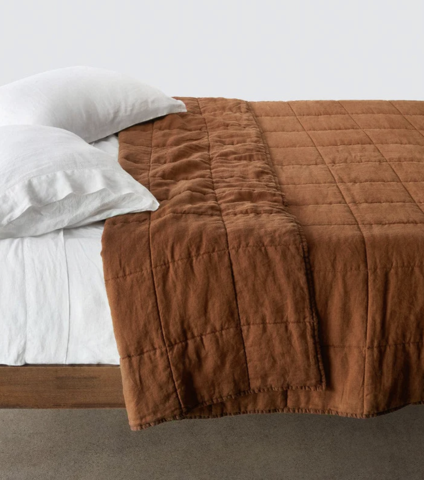 A neatly made bed with white pillows and sheets, featuring a brown quilted blanket folded over the mattress.